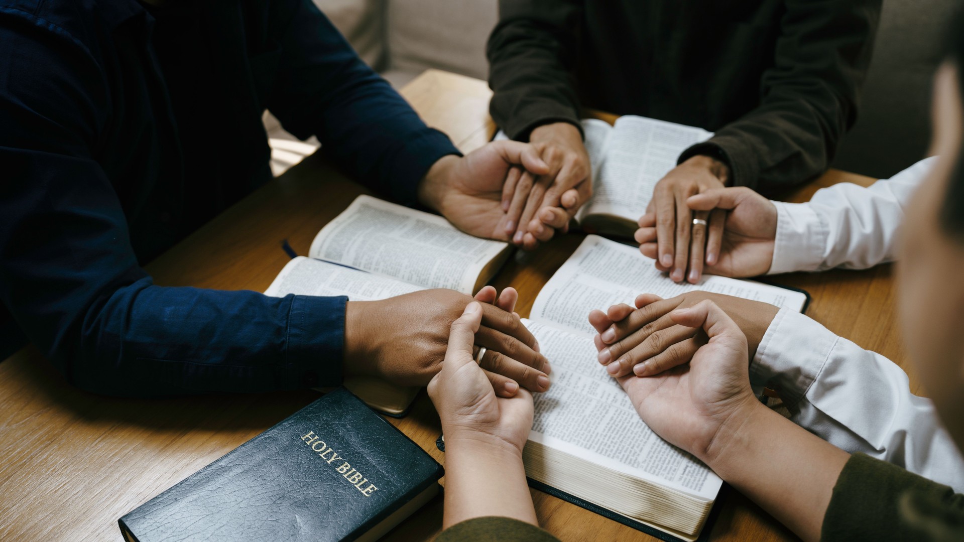 Christian Family prayer and worship. Christian group of people holding hands and praying worships to believe and Bible on a wooden table prayer meeting concept. Church Community pray together