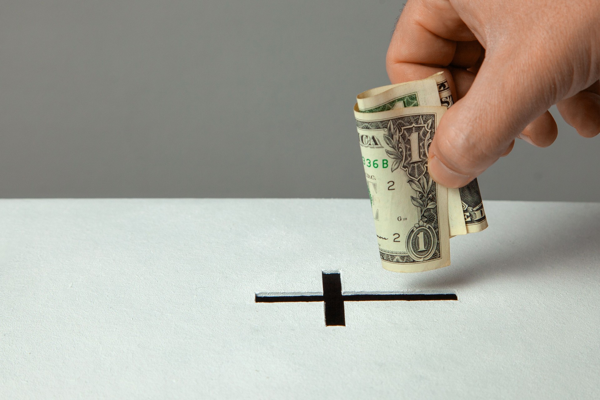 Man puts donation in his hand with dollar in slot in the form of Christian cross. Copy space for text