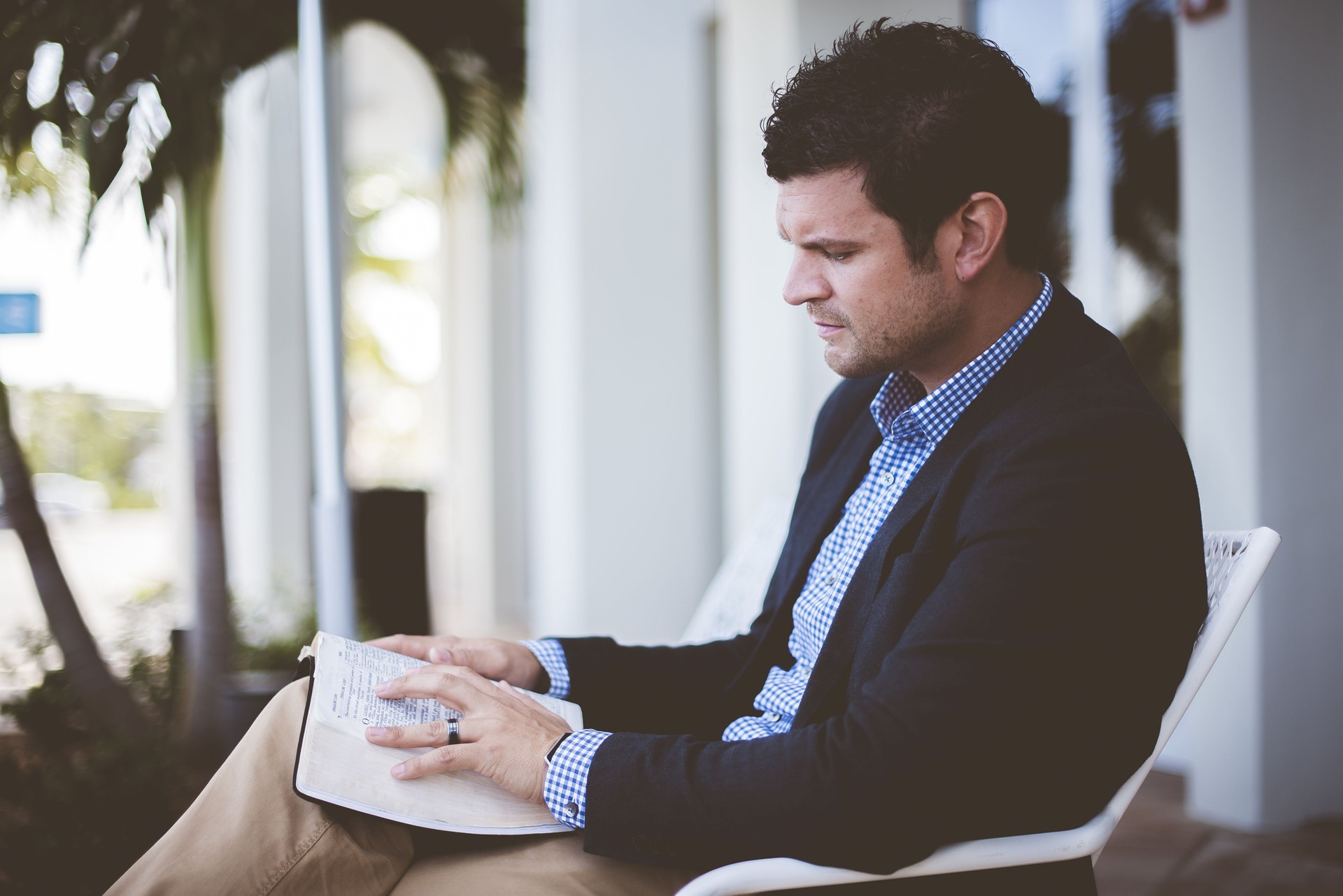 Closeup shot of a male wearing a suit sitting while reading the bible with a blurred background